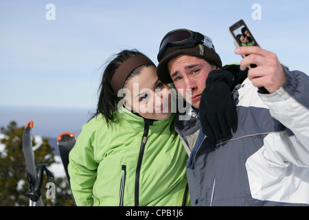 Junges Paar mit einem Fotohandy auf eine Skipiste Stockfoto