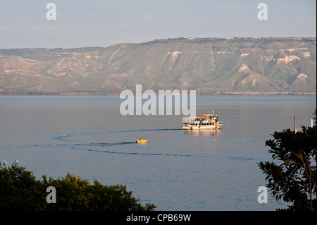 Ausflugsboote navigieren den See Genezareth, wie die Felsen von den Golan-Höhen (besetzten syrischen Gebiet) auf dem jenseitigen Ufer steigen. Stockfoto