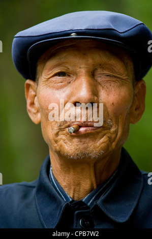 Eine ältere chinesische Mann in traditioneller Kleidung und das Rauchen eine Zigarre posieren für die Kamera in Pingliang gekleidet. Stockfoto