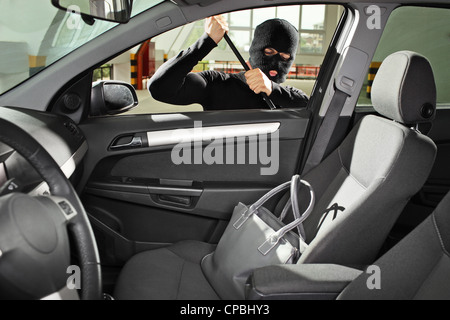 Ein Dieb mit Raub Maske versucht, eine Handtasche Tasche in ein Auto zu stehlen Stockfoto