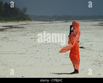 Lokale swahili Frau, die an einem weißen Sandstrand in Sansibar, in Heat Haze mit Sea Breeze ihrer farbenfrohen Tracht flatterte. Stockfoto