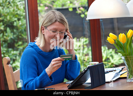 Blonde Frau arbeiten bei Homeshopping auf Linie mit ihrem iPad Tablet-Computer und ein iPhone-smartphone Stockfoto