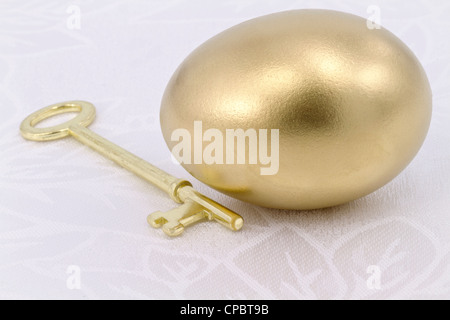 Nahaufnahme eines glänzenden gold-Ei mit glänzenden Schlüssel auf dem weißen Tuch; Metapher des Lösung, Erfolg, Hoffnung und Chance. Stockfoto