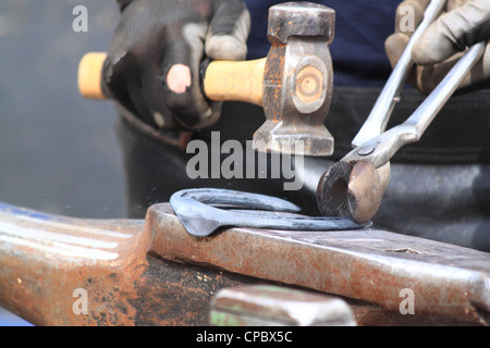 Ein Hufschmied macht ein Hufeisen schlagen mit einem Hammer auf dem Amboss Stockfoto