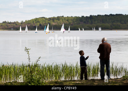 Großvater und Enkel füttern Enten am Frensham Pond mit Segelbooten auf See. Stockfoto