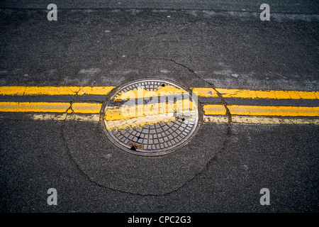 Ein achtlos ersetzte Schachtdeckel unterbricht zwei parallele Linien auf einer Straße in San Clemente, Kalifornien. Stockfoto