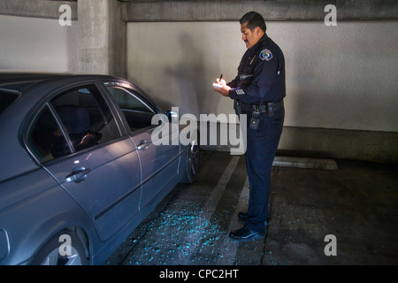 Eine Santa Ana, CA, Hispanic Polizist untersucht ein Auto, das war aufgebrochen und ausgeraubt in einem City-Parkhaus. Stockfoto