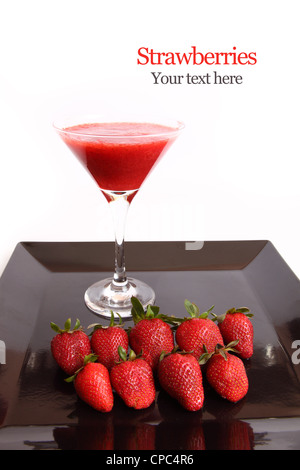 Erdbeersaft in ein Cocktailglas mit frischen Erdbeeren auf schwarze Schale isoliert auf weiß Stockfoto