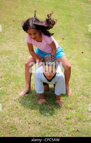Mädchen und Jungen spielen Leapfrog draußen auf der Wiese Stockfoto