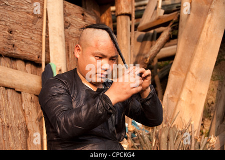 Eine junge Basha Miao (Pistole Männer) Mann seine Haare flechten, nachdem er seine Haare rasiert von einer Sichel, Südchina Stockfoto
