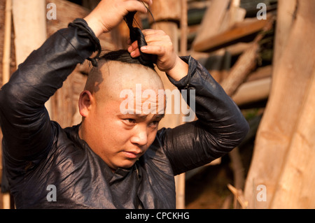 Eine junge Basha Miao (Pistole Männer) Vermittlung von seinem Haar Mann nachdem er seine Haare rasiert von einer Sichel, Südchina Stockfoto