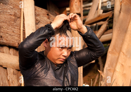 Eine junge Basha Miao (Pistole Männer) Vermittlung von seinem Haar Mann nachdem er seine Haare rasiert von einer Sichel, Südchina Stockfoto