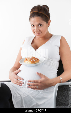 Schwangere Frau Hand in Hand auf dem Bauch und eine Platte mit einem süßen Brötchen auf ihren Bauch Stockfoto