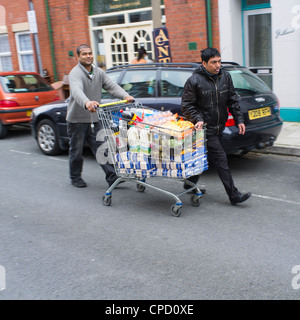 Zwei junge Männer schieben einen shopping trolley voller Essen auf einer Straße, UK Stockfoto