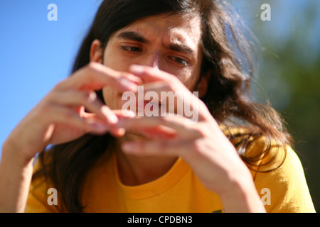 Ein junger Indianer Mann sitzt draußen in der Sonne mit einem nachdenklichen Ausdruck, Hände in der Nähe von Gesicht. Stockfoto