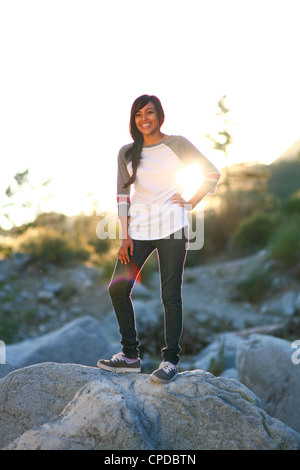 Eine junge Frau multiethnische steht draußen auf einem großen Felsbrocken, die Silhouette von der untergehenden Sonne. Stockfoto