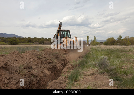 Ein Bagger füllt einen tiefen Graben mit seiner riesigen Schaufel, Eimer in einem ländlichen Gebiet für eine Spülleitung. Stockfoto
