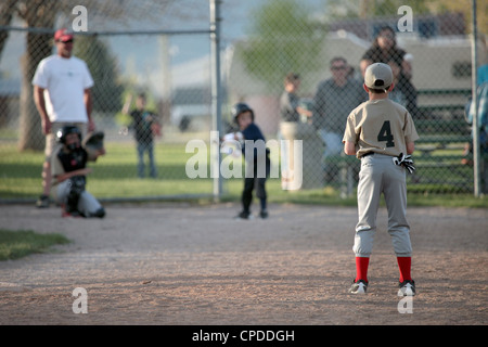 Kleine Liga Baseball Teamplayer junge schlägt Ball und läuft zum ersten Base. Zwei Teams in Uniform. Kleine ländliche Landwirte. Stockfoto