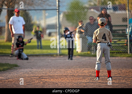 Kleine Liga Baseball Teamplayer junge schlägt Ball und läuft zum ersten Base. Zwei Teams in Uniform. Kleine ländliche Landwirte. Stockfoto