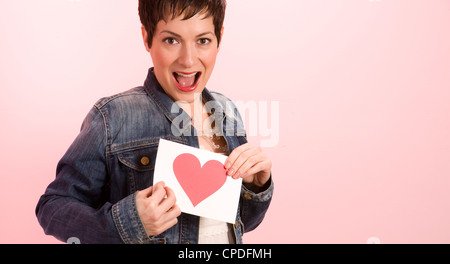 Eine hübsche Frau gegen rosa halten sie ihren Valentinstag Karte mit Herz Stockfoto