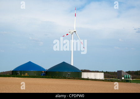 Unterschiedliche Fermenter einer Biogasanlage mit Windmühle im Hintergrund Stockfoto