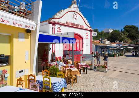 Restaurant am Meer am Hafen im Zentrum von Alvor mit Rettungsstation hinter, in der Nähe von Portimao, Algarve, Portugal Stockfoto