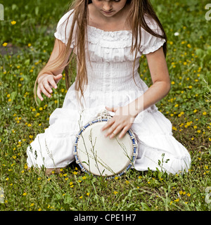 ein Mädchen sitzt auf einer Wiese und spielt Djembe Stockfoto