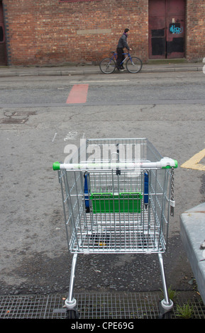 Ein Einkaufswagen in einem leicht laufen aufgegeben ASDA äußeren Stadtzentrum Street in Manchester. Ein Radfahrer ist vorüber. Stockfoto