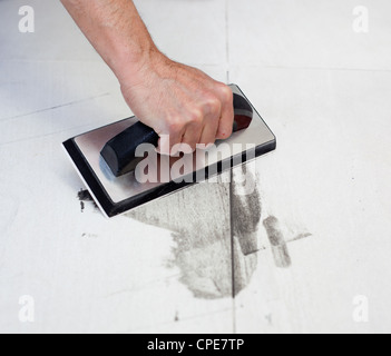 Verfugen der Fliesen mit Gummi-Spachtel und grauem Zement-Mörtel Stockfoto