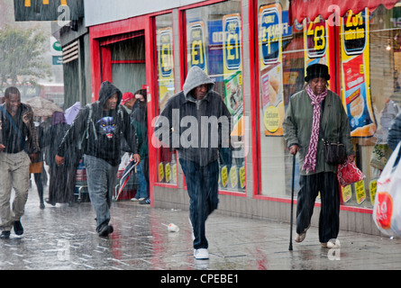 Menschen eilen durch die Straßen von Lewisham im Regen Sturm mit Sonnenschirmen Stockfoto