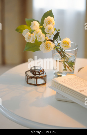 Weiße Rosen im Glas mit offenen Buch auf Tisch Stockfoto