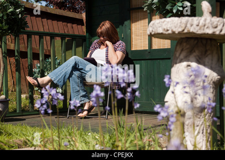 Frau liest eine Kindle e-Reader saßen draußen ihr Sommerhaus in voller Sonne. Stockfoto