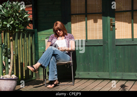 Frau liest eine Kindle e-Reader saßen draußen ihr Sommerhaus in voller Sonne. Stockfoto