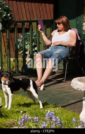 Frau liest eine Kindle e-Reader saßen draußen ihr Sommerhaus in voller Sonne. Stockfoto