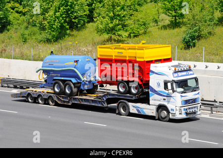 Knickgelenkter Lader für den Transport neuer farbenfroher Landmaschinen von Agrimac hinter einem Volvo LKW-Transportunternehmen, das entlang der M25 Essex England UK fährt Stockfoto