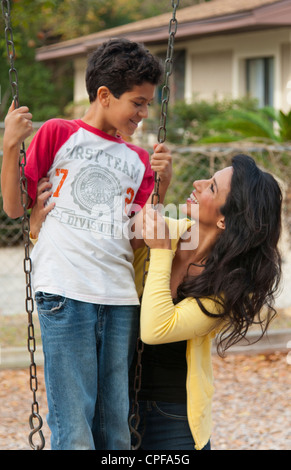 Hispanische alleinerziehende Mutter und Som Alter 11 auf Schaukel im Park am Spielplatz in der Nähe von zu Hause im freien Stockfoto