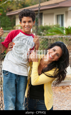 Hispanische alleinerziehende Mutter und Som Alter 11 auf Schaukel im Park am Spielplatz in der Nähe von zu Hause im freien Stockfoto