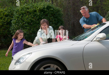 Vater und Mutter und Töchter Familie Autowaschen zu Hause in Einfahrt zusammen mit Schlauch und Spaß Stockfoto