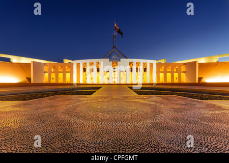 Parliament House, Canberra, Australien, in der Dämmerung beleuchtet. Aborigine-Mosaik im Vordergrund, ist australische Flagge. Stockfoto