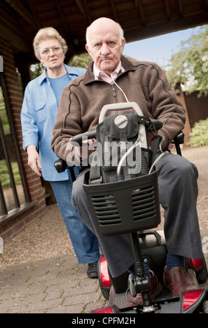 Älteres Paar, für einen Spaziergang, während man einen motorisierten Mobilität Roller fährt Stockfoto