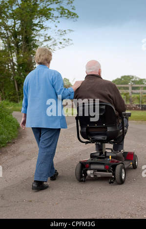 Reife Ehepaar glücklich heraus für einen Spaziergang auf dem Lande während man einen motorisierten Mobilität Roller fährt Stockfoto