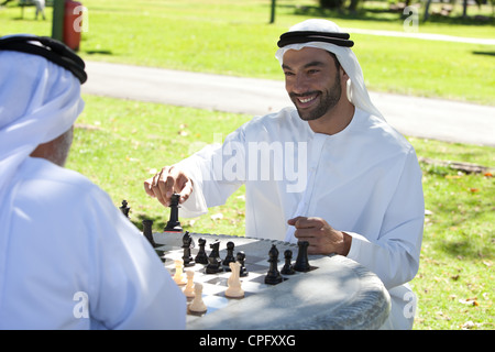 Arabische erwachsener Sohn spielt Schach mit Vater im Park, lächelnd. Stockfoto