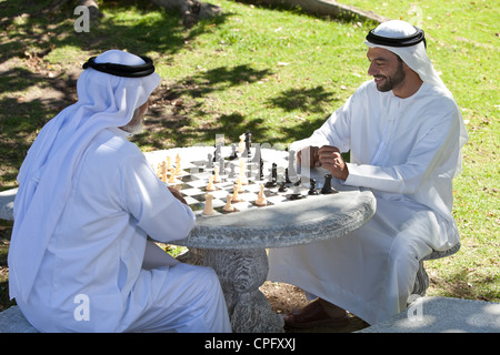 Arabische erwachsener Sohn spielt Schach mit Vater im Park, lächelnd. Stockfoto