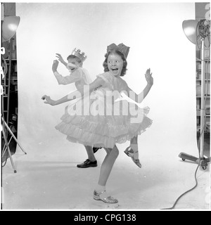 Noch aus den sechziger Jahren, die mit zwei kleinen Kindern Adverting gekleidet in Party-Outfits und Hüte tanzen in ein Fotostudio. Stockfoto