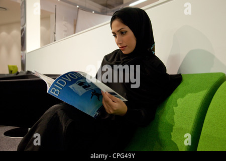 Arabische Frau sitzt auf dem Sofa und lesen Magazin. Stockfoto