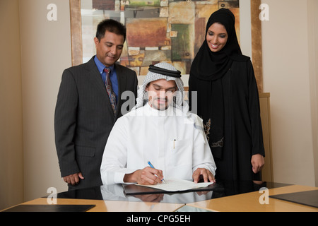 Arabische Geschäftsmann unterschreiben, zwei Kollegen, die auf der Seite stehen. Stockfoto