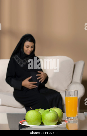 Saft Glas und grüner Apfel auf Tisch, während schwangere Frau sitzen im Hintergrund gehalten Stockfoto