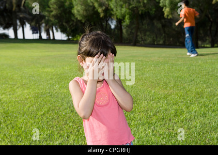 Mädchen für Gesicht mit den Händen im Park, während junge im Hintergrund Stockfoto