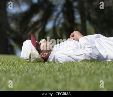 Junger Mann auf dem Rasen liegen und Musik hören Stockfoto