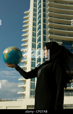 Arabische Frau hält einen Globus, stehend mit Hintergrund des Gebäudes in Dubai Marina, Vereinigte Arabische Emirate Stockfoto